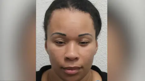 West Midlands Police A woman with pulled-back black curly hair looking at the camera in a police mugshot. She is wearing a black top and small gold nose ring.