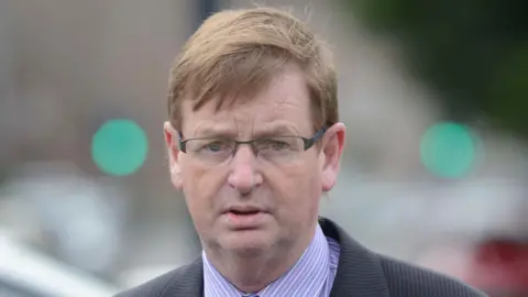 Willie Frazer outside with short brown hair and wearing a dark suit with a purple shirt 