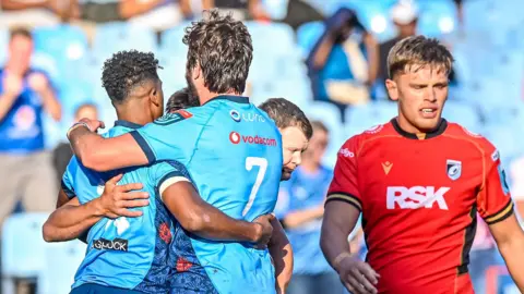 Bulls players celebrate as Cardiff's Alex Mann walks past
