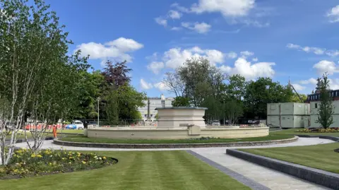 Richard Madden/BBC A view of the Rose Bowl and fountain in Hull as construction work takes place in Queen's Gardens, Hull. The cream coloured fountain stands in the centre of the image surrounded by a circular path and large, raised lawns and flower beds. Construction workers are visible in the background. Hull College and the statue of William Wilberforce, which stands on a large plinth, can be viewed through a gap in the trees.