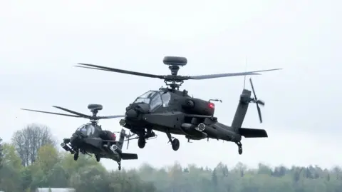 Two helicopters flying above the trees