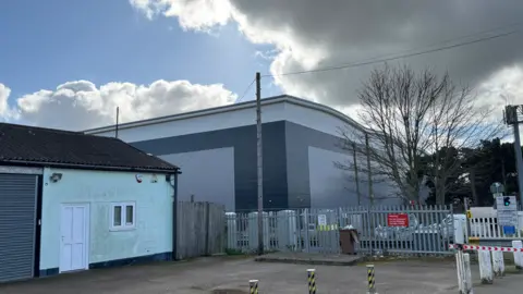 George King/BBC The corner of the warehouse can be seen next to a smaller building and just behind a railway