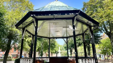 The image shows the bandstand in the centre of Redditch, with the sun shining. 