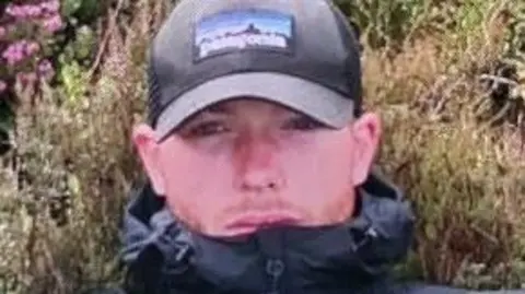 Police Scotland Shane Donnelly or Barr, a young man wearing a black cap and black jacket with visible stubble on his face