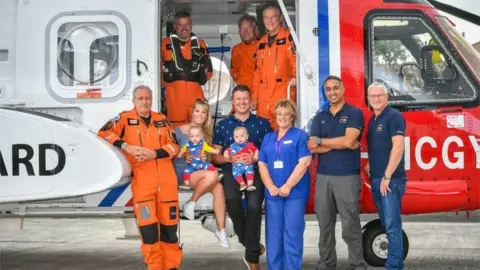 PA Media The family reunited with midwife Jane Parke and coastguard helicopter crew members who helped them