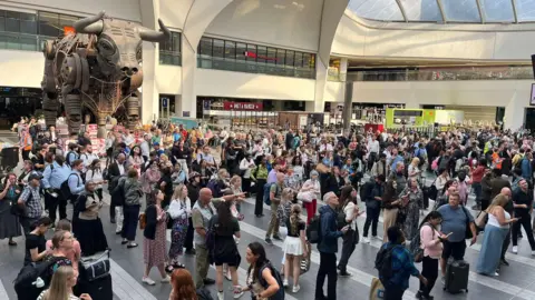 A crowded train station with a statue of a metal bull in the background.