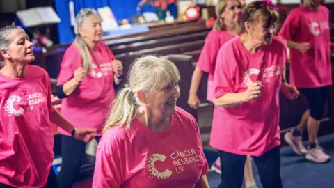 Gray Walker/ Scenicview Gallery & Studio Women in pink t-shirts dance in the zumbathon