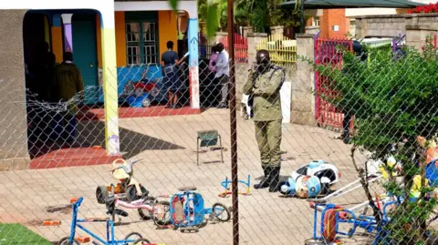 An Ugandan police officer secures the scene at a school after a man posing as a parent stabbed and killed children there, in Kampala, Uganda