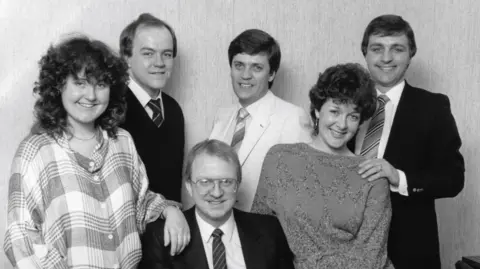 A black and white picture of the above named people. They are all dressed smartly and smiling. All are standing up except for Gavin McCoy, who is sitting.