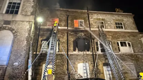 Ryde former theatre and town hall with smoke coming from the building and flames from the windows - firefighters are on ladders and at street level fighting the fire.