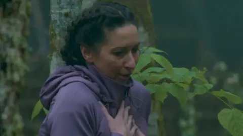 BBC/Studio Lambert The Traitors' Rachel is left terrified as a hand appears from the ground. She is wearing a purple coat and has shoulder length, dark hair tied back. She has her hands on her chest to show she is surprised.