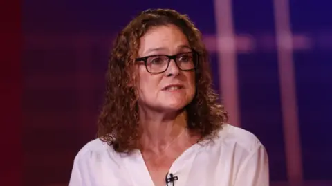 A general view of Jo Boydell, who is wearing a white shirt. She has brown, shoulder length hair and is wearing dark glasses.