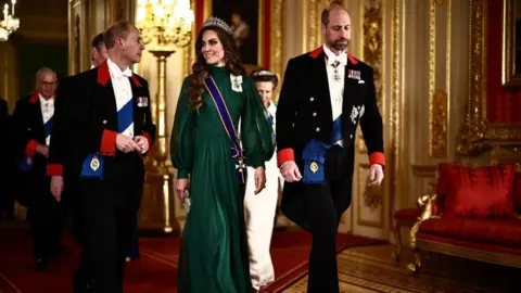 PA Media The Duke of Edinburgh in a black suit walks alongside the Princess of Wales who is wearing a green, long-sleeve floor-length gown and tiara with the Prince of Wales next to her in a black suit