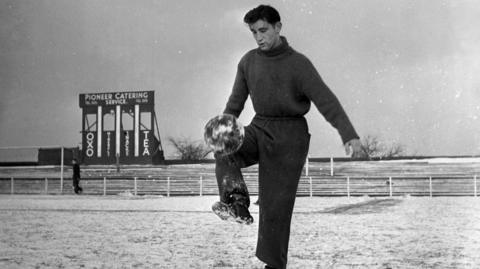 Geoff Twentyman plays with football in snow, 1951.
