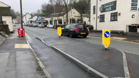 A view of a built-out section near a building signed Community Hub with obvious damage to the corner kerb stone