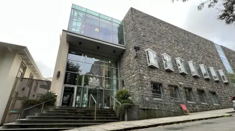 BBC The image shows Guernsey's Royal Court. It has a glass entrance next to some paved steps.