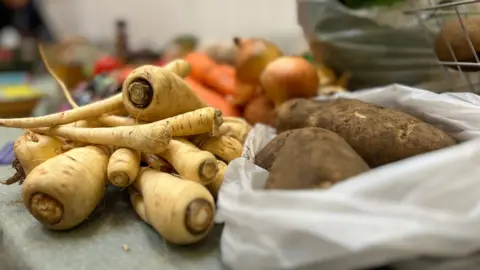 A close up of parsnips, carrots, potatoes and onions laid on a table.