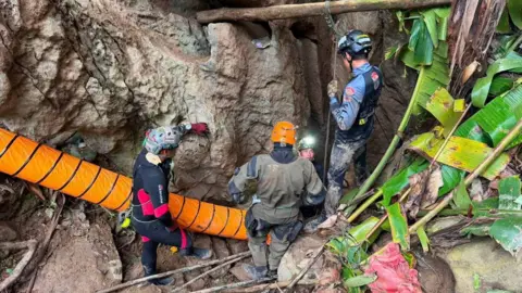 Four rescuers are seen from above standing among rocks. 