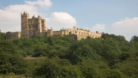 Getty Images A view of Bolsover Castle - an ornate tower and associated ruined buildings - seen from slightly below looking up at its position on a steep wooded hill