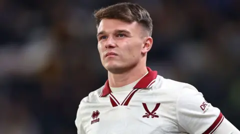 Getty Images Jamie Shackleton, who is wearing a predominantly white Sheffield United jersey with red trim, including a red logo of two swords crossing.