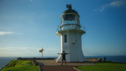 RUSS COOK A man stood with blue skies and sea behind him.