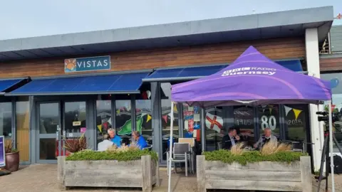 A purple topped gazebo with BBC Radio Guernsey on it in front of Vistas Café.