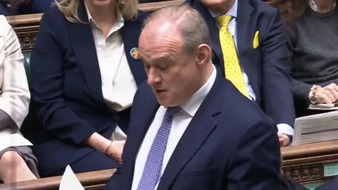 PA Media A screen grab of Liberal Democrats leader Sir Ed Davey speaking during Prime Minister's Questions in the House of Commons. He has short grey hair and is wearing a dark blue suit with a white shirt and a blue patterned tie. 