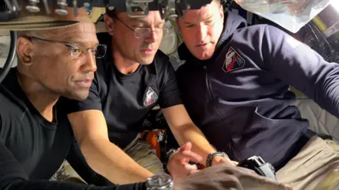 NASA Artemis II Pilot Victor Glover, Commander Reid Wiseman, and Mission Specialist Jeremy Hansen prepare for their journey around the far side of the Moon by configuring their camera equipment shortly before beginning their lunar flyby observations.