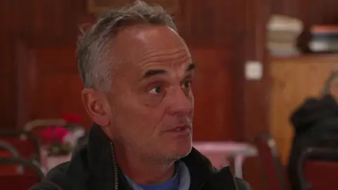 Simon Gleave, chairman of Adlington Parish Council, has short grey hair. He is wearing a dark jacket over a blue top.