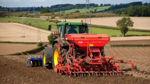 A red and green tractor is ploughing a field