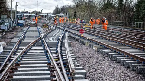 Govia Thameslink Workers in orange hi vis and white hard hats work on a closed section of railway line.