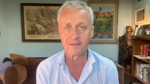 Hugh Schofield faces the camera from a living room