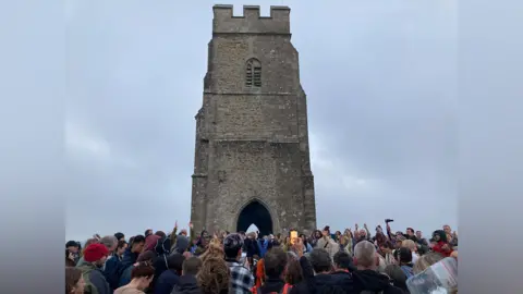 Crowd around the base of Glastonbury Tor with a grey sky