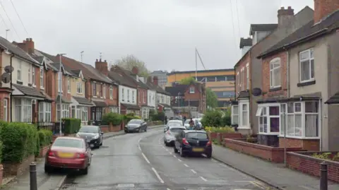 Staveley Road. It is a residential road with houses either side. Molineux Stadium is at the end. There are cars either side. 