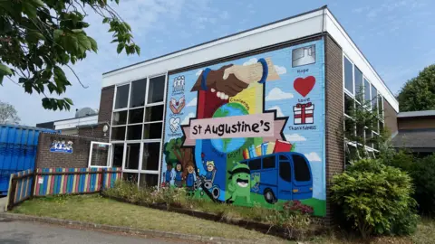 A colourful mural on the side of the school building shows two shaking hands, the book bus and says "St Augustine's" on it.