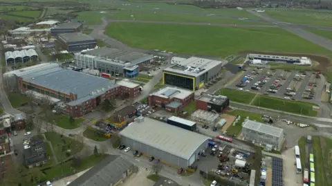 Cranfield University Cranfield University campus with its airport in the background and large buildings with car parks in the foreground.
