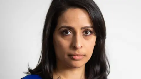 BMA Dr Patel is looking directly at the camera. She has shoulder length dark hair and is wearing a bright blue top. She is in front of a grey background.