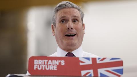 Keir Starmer looking surprised from behind a sign that says 'Britain's future'