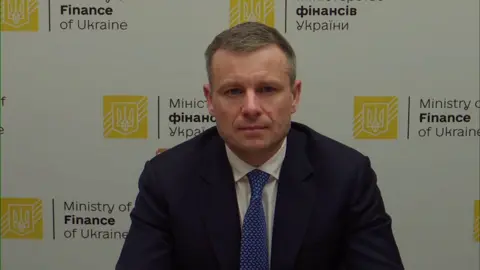 Ukraine's finance minister Sergii Marchenko wearing a navy jacket, white shirt and blue tie as he looks into the camera