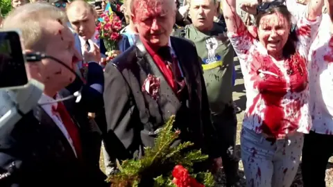 Polish ambassador to Russia covered in red liquid and surrounded by a crowd