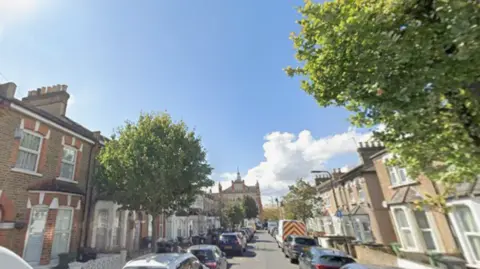 General view of Saint George’s Road. The road is lined by Victorian terraced houses, a couple of trees and cars parked on both sides