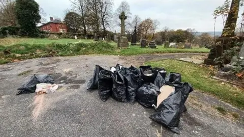 Bradford Council Several black bags filled with rubbish and dumped on a path in a cemetery.