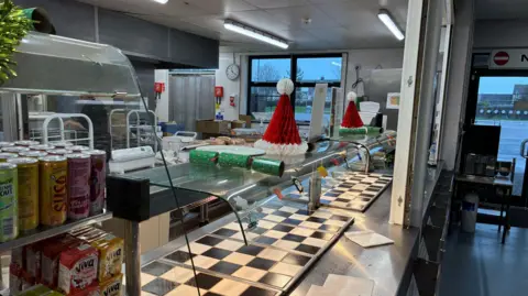 Školní jídelna s černými a bílými plotýnkami. Sušenky, slavnostní klobouky a lednice s nealkoholickými nápoji jsou také vidět s dveřmi vedoucími ven úplně vpravo.