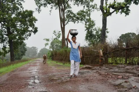 WaterAid/Ronny Sen A girl carrying water back to her home.