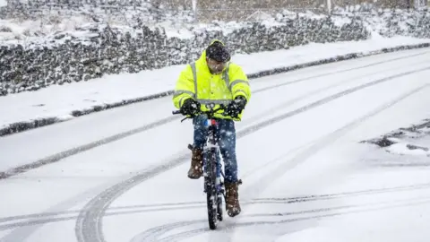 PA A man rides a bike in snowy conditions in Hawes in the Yorkshire Dales National Park
