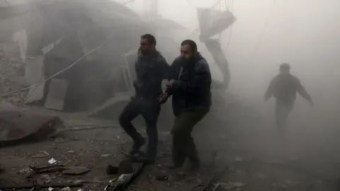 AFP A wounded man is helped from the scene of a reported government air strikes on the town of Arbin, in the besieged rebel-held Eastern Ghouta (8 February 2018)