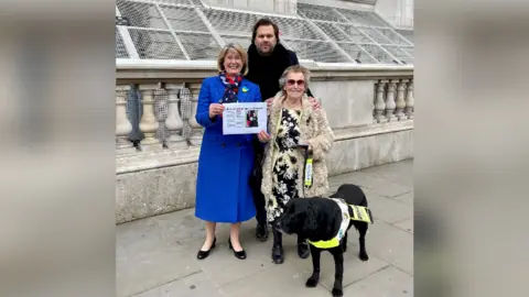 Anna Firth MP Anna Firth, BBC local radio presenter Justin Dealey, and Jill Allen-King with her guide dog Jagger