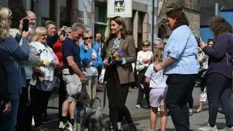 PA Media Kate, wearing a tweed jacket and carrying a posy of yellow and blue flowers chats to the crowds in Tobermory