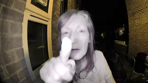 Still from doorbell camera footage shows neighbour Drina staring straight ahead and pointing her finger