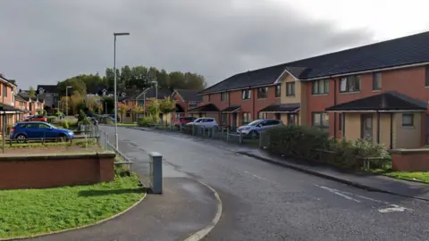 A cul-de-sac in Glasgow with a row of red brick homes, with cars parked in front of each one.